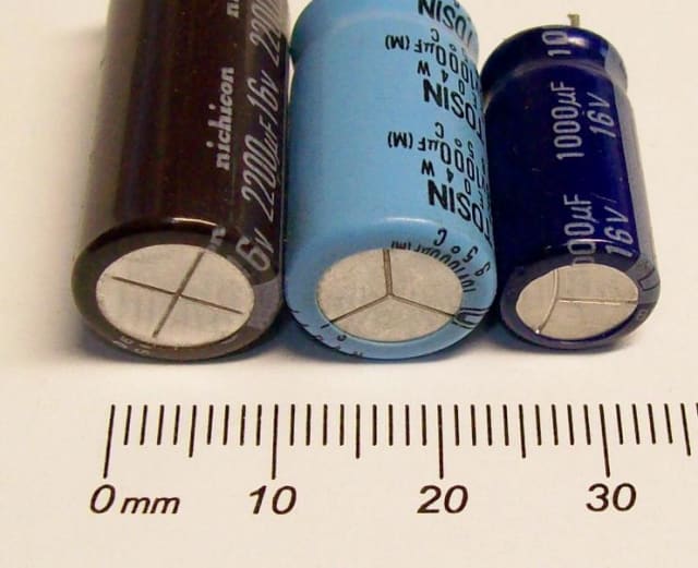 Pressure relief vents on three electrolytic capacitors. (Image: Wikimedia / Ulfbastel.)