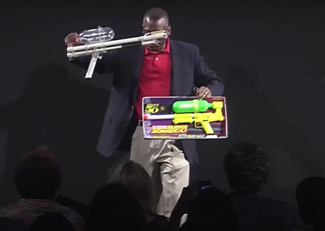 Lonnie Johnson holds up his original Super Soaker prototype alongside a commercial version in a 2014 TEDx Talk. (Image: TEDx Talks.)